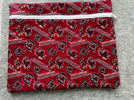 A folded fabric item, likely a pouch or sleeve, featuring a repeating South Carolina Gamecocks print in red, black, white, and yellow on a gray textured background.