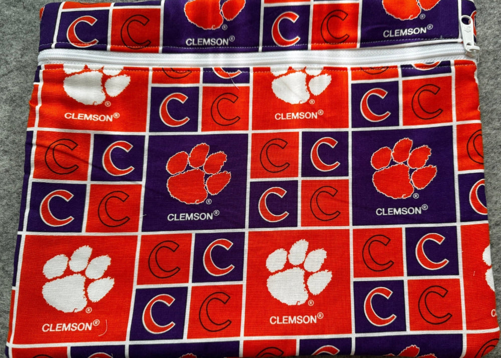 A folded fabric item, likely a pouch or small bag, featuring a repeating Clemson Tigers block pattern in red, purple, and white, laid flat on a gray textured background.